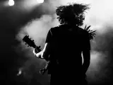 Muzyk z rozwianymi włosami gra na gitarze, w dymie i świetle sceny. Energia gatunku rockowego w czerni i bieli.