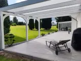 Moderne Terrasse bauen: Überdachter Sitzbereich mit Liegestuhl, Grill und Blick ins Grüne.