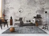 Salon w stylu minimalistycznym z szarą sofą, czarnym fotelem i dywanem. Na ścianie betonowa faktura.