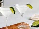 Dwa kieliszki z białym drinkiem, ozdobione plasterkami limonki. Obok miseczka z limonkami i shaker. Idealny kamikaze shot na gorący wieczór.