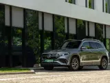 Nowy Mercedes 4x4, elegancki SUV, zaparkowany przed nowoczesnym budynkiem z zielonymi odbiciami drzew w szybach.