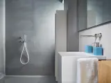 Bagno moderno con rivestimento doccia senza piastrelle effetto resina, lavabo bianco e accessori azzurri.