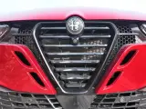 Czerwona Alfa Romeo z bliska. Widoczny grill w kształcie tarczy z logo, reflektory i detale karoserii w zbliżeniu. Alfa makro.