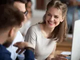 Lachende Frau im Büro, die mit Kollegen über ein Projekt spricht. Sie engagiert sich im volontariat journalismus und teilt Ideen.