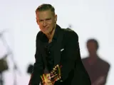Bryan Adams w czarnym garniturze gra na gitarze. Sprawdź jego nadchodzące wydarzenia i koncerty.