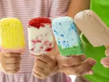 Vier Kinderhände halten bunte Eis am Stiel. Ein gelbes, ein Erdbeer-Vanille, ein blau-grünes und ein Schokoladen-Eis. Perfekt für heiße Tage!