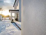 Biały, ziarnisty tynk na elewacji domu w zimowej scenerii. Idealny wybór, jeśli zastanawiasz się, jaki tynk na elewację wybrać, by wyglądała nowocześnie i estetycznie.