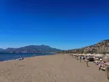 Słoneczna plaża w Sarigerme, z turkusowym morzem, górami w tle i rzędami leżaków pod słomianymi parasolami.