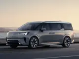 Szary Volvo EM90 jedzie wzdłuż wybrzeża o zachodzie słońca.