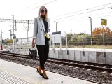 Elegancka kobieta w szarej marynarce i czarnych spodniach czeka na pociąg.