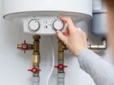Adjusting the temperature dial on a water heater, showing its plumbing connections.