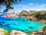 Turkusowa woda i skaliste wybrzeże Costa Smeralda na Sardynii. Kilka łodzi kołysze się na falach.