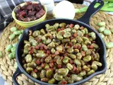 Habas tiernas salteadas con trocitos de jamón en una sartén de hierro fundido, un plato tradicional lleno de sabor.