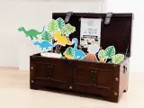 Coffre en bois rempli de décorations de dinosaures et de feuilles tropicales.