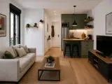 Un loft pequeño moderno con sofá beige, mesa de centro de madera, cocina verde y TV.
