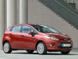 Czerwony Ford Fiesta MK6 zaparkowany przed nowoczesnym budynkiem z betonowymi kolumnami i schodami.