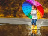 Radosna dziewczynka w żółtych kaloszach skacze po kałużach z tęczowym parasolem. Świetny pomysł, gdzie pojechać z dzieckiem, gdy pada deszcz!
