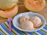 Tre palline di cremoso gelato al melone in una ciotola bianca, con fette di melone fresco sullo sfondo.