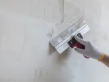 Ręka w rękawicy wykonuje szpachlowanie ścian, wygładzając nierówności.