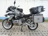 Srebrny motocykl BMW R1200GS z kuframi i torbą na bak. Wady tego modelu to m.in. wysoka cena i skomplikowana elektronika.