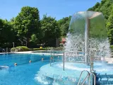 Erfrischender Brunnen im Naturbad Elbingerode, umgeben von grünen Bäumen und blauem Wasser.