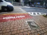 Czerwony pas na chodniku z napisem "UWAGA POJAZDY" informuje o przejściu sugerowanym. W tle widać samochody i schody.