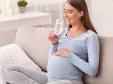 Uśmiechnięta ciężarna kobieta pije wodę, dbając o siebie podczas ciąży. Krzywa cukrowa w ciąży wymaga troski.