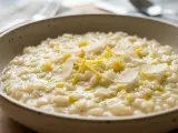 Un cremoso risotto al limone, guarnito con scorza di limone e scaglie di parmigiano, pronto per essere gustato.