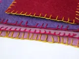 Tessuti colorati sovrapposti, rifiniti con un punto coperta giallo, rosa e rosso.