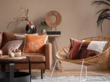 Un salon cosy avec un canapé en cuir marron, des coussins aux motifs ethniques et une chaise en rotin.