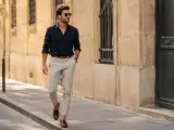 Mężczyzna w granatowej koszuli i beżowych spodniach, prezentujący styl smart casual, spaceruje ulicą.