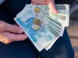 Ręce trzymają polskie banknoty 50 i 100 zł oraz monety. To może być kwota na bon oświatowy.
