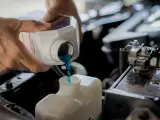Hands pour blue coolant into a car's reservoir. This maintenance task is essential for preventing overheating, which can lead to costly car radiator replacement.