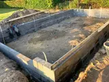 Byggarbetsplats med ett mura grund av betongblock. Schakt, spade och vattenpass syns.