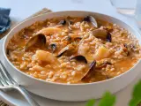 Un delicioso arroz caldoso de marisco, repleto de gambas, mejillones y almejas, servido en un cuenco blanco.