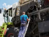 Mechanik na drabinie naprawia kombajn. Co to jest tuz? To potężna maszyna rolnicza, która zbiera plony.