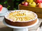 Torta di mele velocissima in 10 minuti, decorata con fettine di mela e zucchero a velo. Sullo sfondo, una cassetta di mele rosse e gialle.