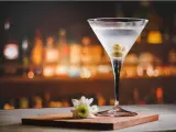 Eleganckie martini z colą, ozdobione oliwkami, na tle rozmytego baru. Obok kieliszka leży biały kwiatek.