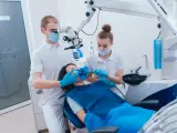 Dentysta pod mikroskopem bada ząb pacjentki, by wykluczyć zatrucie zęba. Asystentka przygotowuje narzędzia.
