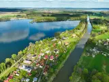 Pławniowice jezioro otoczone zielenią i domkami letniskowymi, z kanałem wodnym biegnącym wzdłuż brzegu.