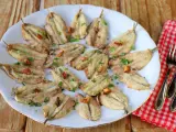 Un plato blanco con boquerones fritos, dorados y crujientes, espolvoreados con perejil fresco y trocitos de ajo.