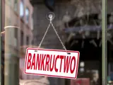 Tabliczka "BANKRUCTWO" wisząca na łańcuszku na szybie.