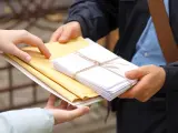Listonosz przekazuje koperty. Zastanawiasz się, ile zarabia listonosz za taką pracę?