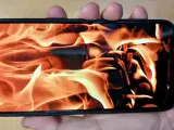 En hand håller en iPhone med en flammande eld som bakgrundsbild. Det ser ut som att iphone blir varm.