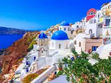 Santorini wakacje: białe domy z niebieskimi kopułami na zboczu klifu nad lazurowym morzem. Idealne miejsce na wymarzone wakacje.