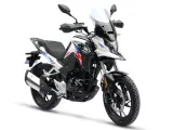 Nowy motocykl gotowy do docierania. Biało-czarny z czerwono-niebieskimi akcentami, z wysoką szybą i terenowymi oponami.