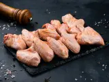 Skrzydełka kurczaka gotowe do pieczenia, zamarynowane w aromatycznej solance. Obok młynek do pieprzu i gruboziarnista sól.