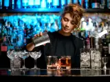 Barman nalewa drink z shakera do szklanki, w tle półki z butelkami i niebieskie światła.