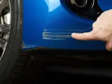 Dito, un dito indica profondi graffi sul parafango blu di un'auto, segno che necessita di riparazione vernice auto.
