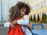 Zwei Kinder umarmen sich. Ein Mädchen mit Locken lächelt in die Kamera. Ein schönes Beispiel für Empathie bei Kindern.